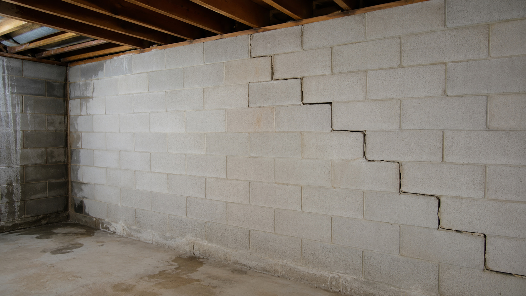Stair-step cracking in a basement block wall with signs of foundation stress and moisture exposure